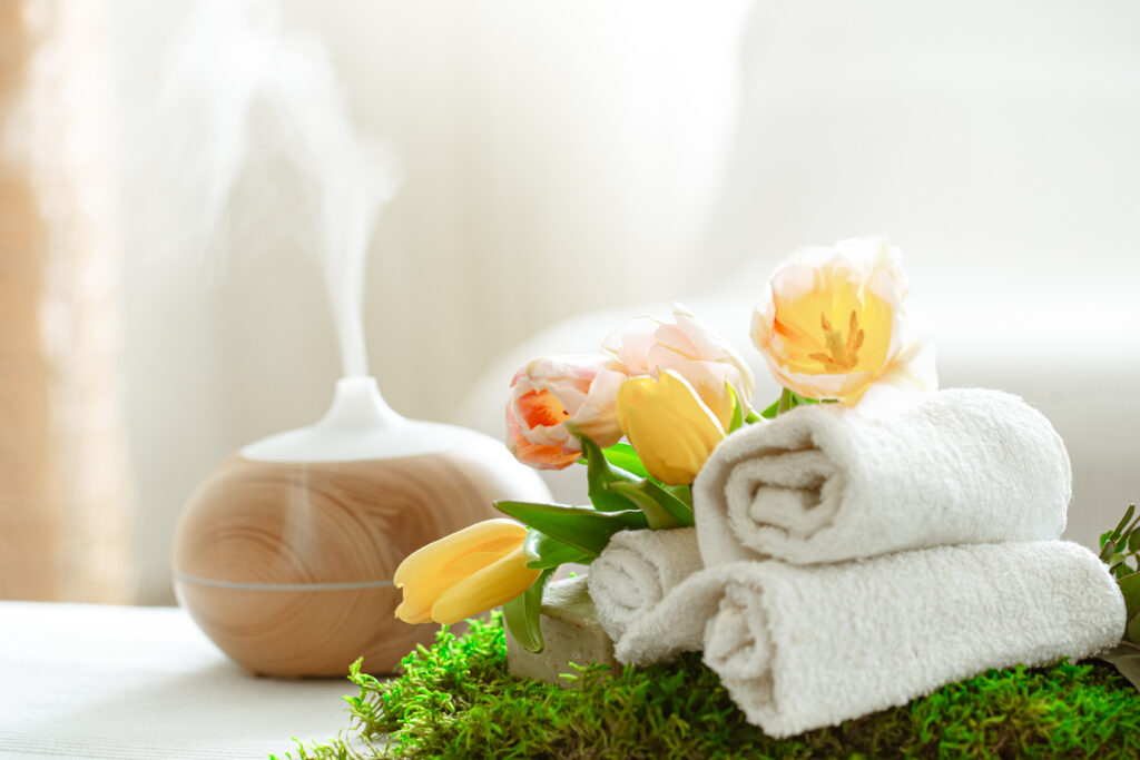 Spa composition with the aroma of a modern oil diffuser with body care products . Twisted white towels, spring greens and flowers. Spa concept for body and health care .