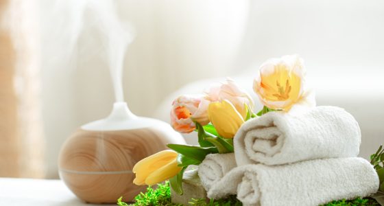 Spa composition with the aroma of a modern oil diffuser with body care products . Twisted white towels, spring greens and flowers. Spa concept for body and health care .